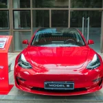 A stylish red Tesla Model 3 parked in an urban area, showcasing its sleek design and luxury features.
